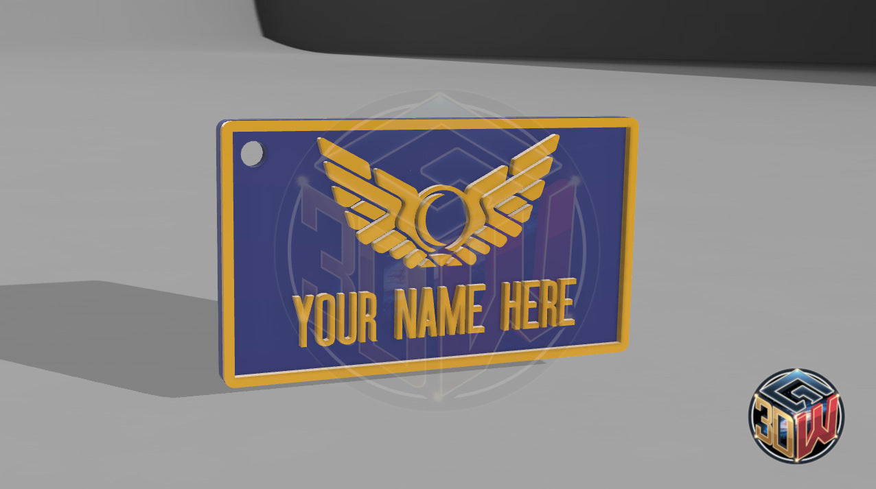 3D-printed, blue and gold name tag with a space-themed design, featuring a winged emblem and customizable text area labeled 'Your Name Here.' The tag is rectangular, lightweight, and is a computer render.