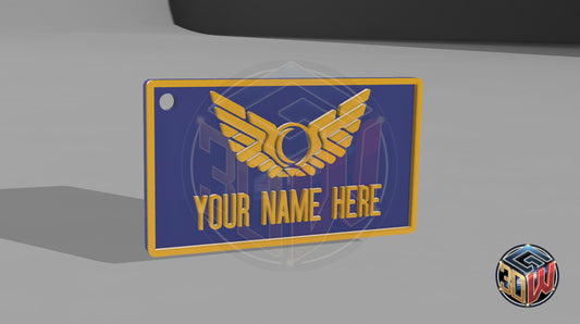 3D-printed, blue and gold name tag with a space-themed design, featuring a winged emblem and customizable text area labeled 'Your Name Here.' The tag is rectangular, lightweight, and is a computer render.